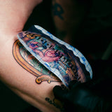 Tattoo artist applying a colorful tattoo design on a person's arm.